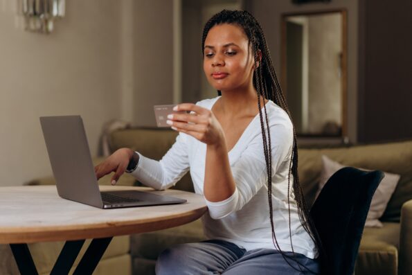 Entenda como alugar um imóvel utilizando o cartão de crédito: Foto de uma mulher preta segurando um cartão em frente ao notebook